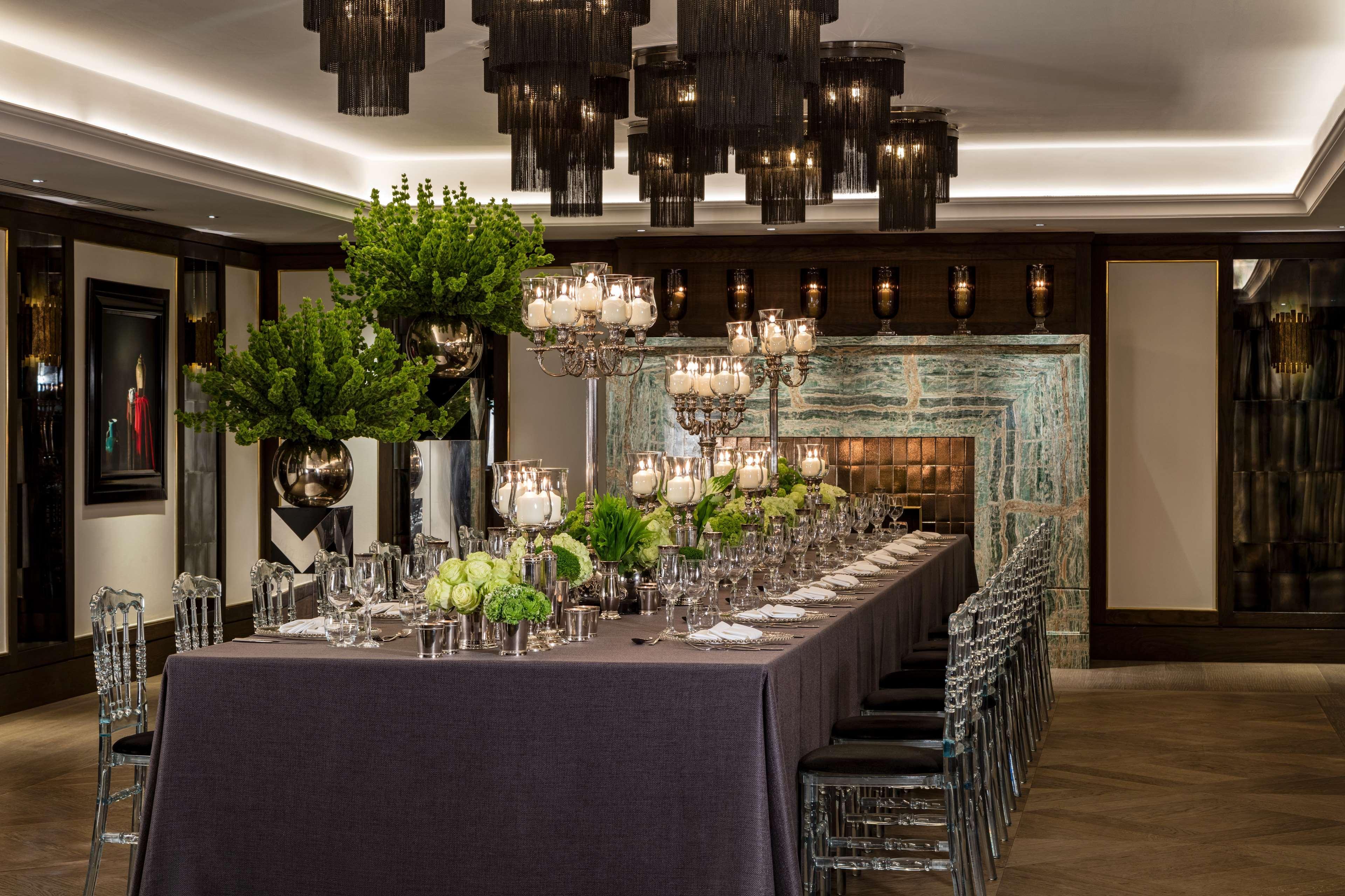 The May Fair, A Radisson Collection Hotel, Mayfair Londres Extérieur photo The photo shows a sophisticated dining setting. A long table is elegantly arranged with a dark tablecloth and decorative centerpieces that include lush greenery and ornate candle holders. The table is set with glassware and tableware, indicating it i