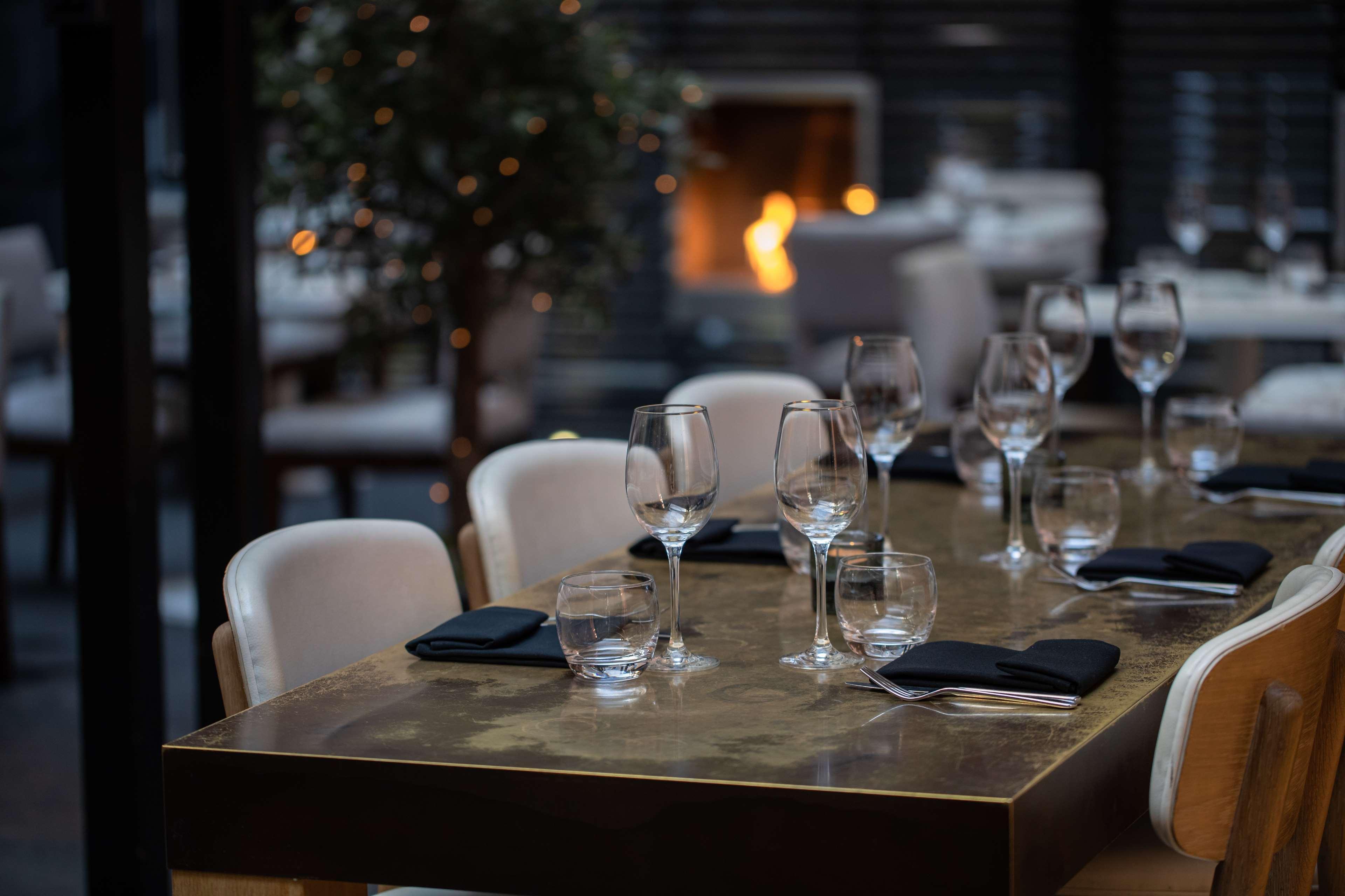The May Fair, A Radisson Collection Hotel, Mayfair Londres Extérieur photo The photo shows a stylish restaurant dining area. A beautifully set table is in the foreground, featuring elegant glassware and black napkins. The table has a glossy surface and appears to be well-prepared for dining. In the background, there is a co