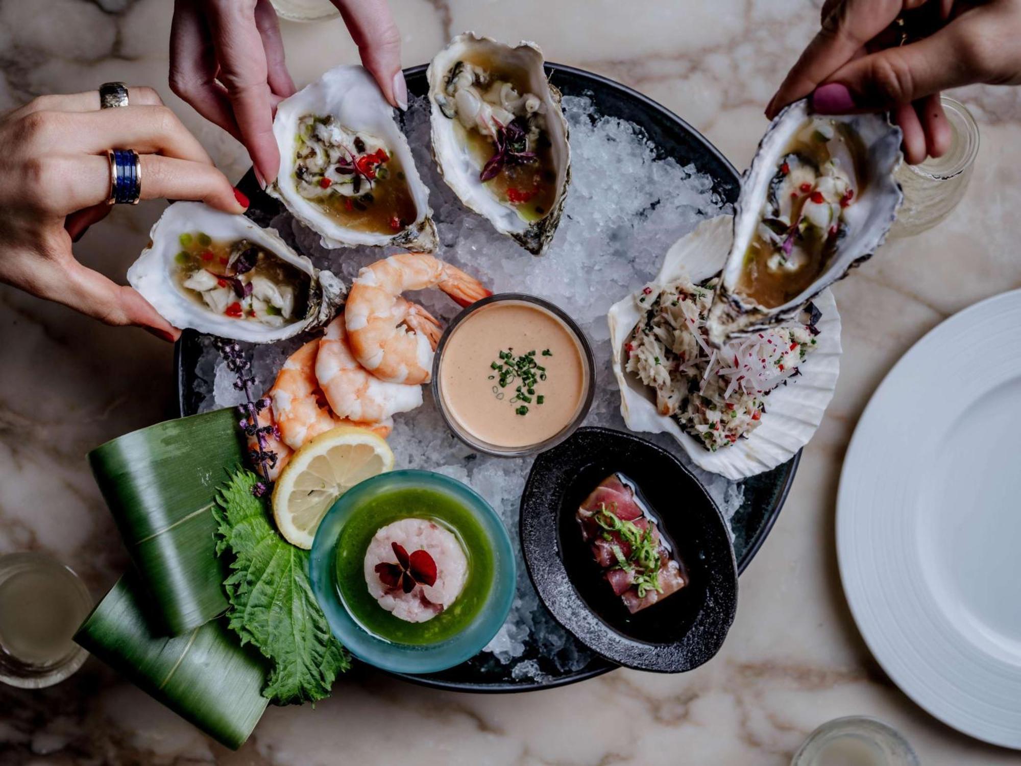 The May Fair, A Radisson Collection Hotel, Mayfair Londres Extérieur photo The photo displays a seafood platter arranged beautifully on a round dish filled with ice. Various types of seafood are presented, including several open oysters topped with garnishes, shrimp, and a small dish of sauce in the center. Surrounding the 